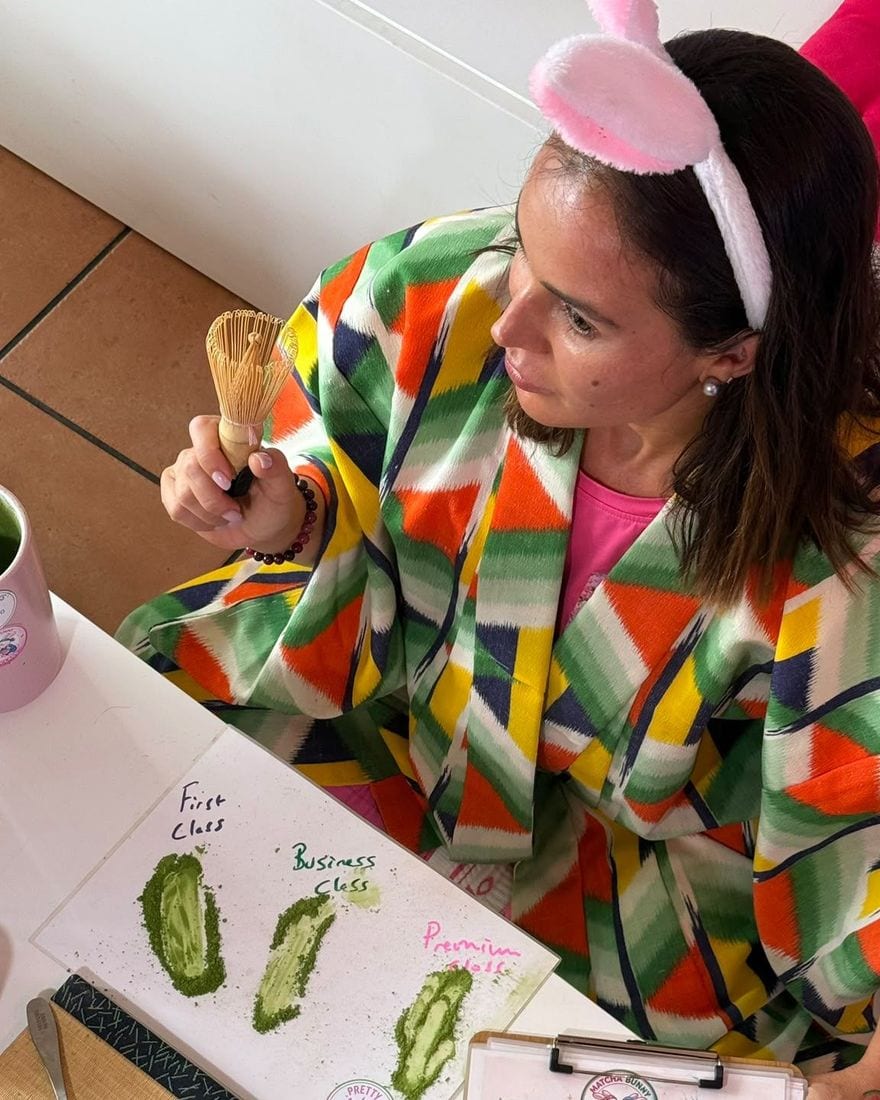 Selin Uncuoglu in a colourful kimono and bunny ears, holding a bamboo whisk above the three grades of matcha